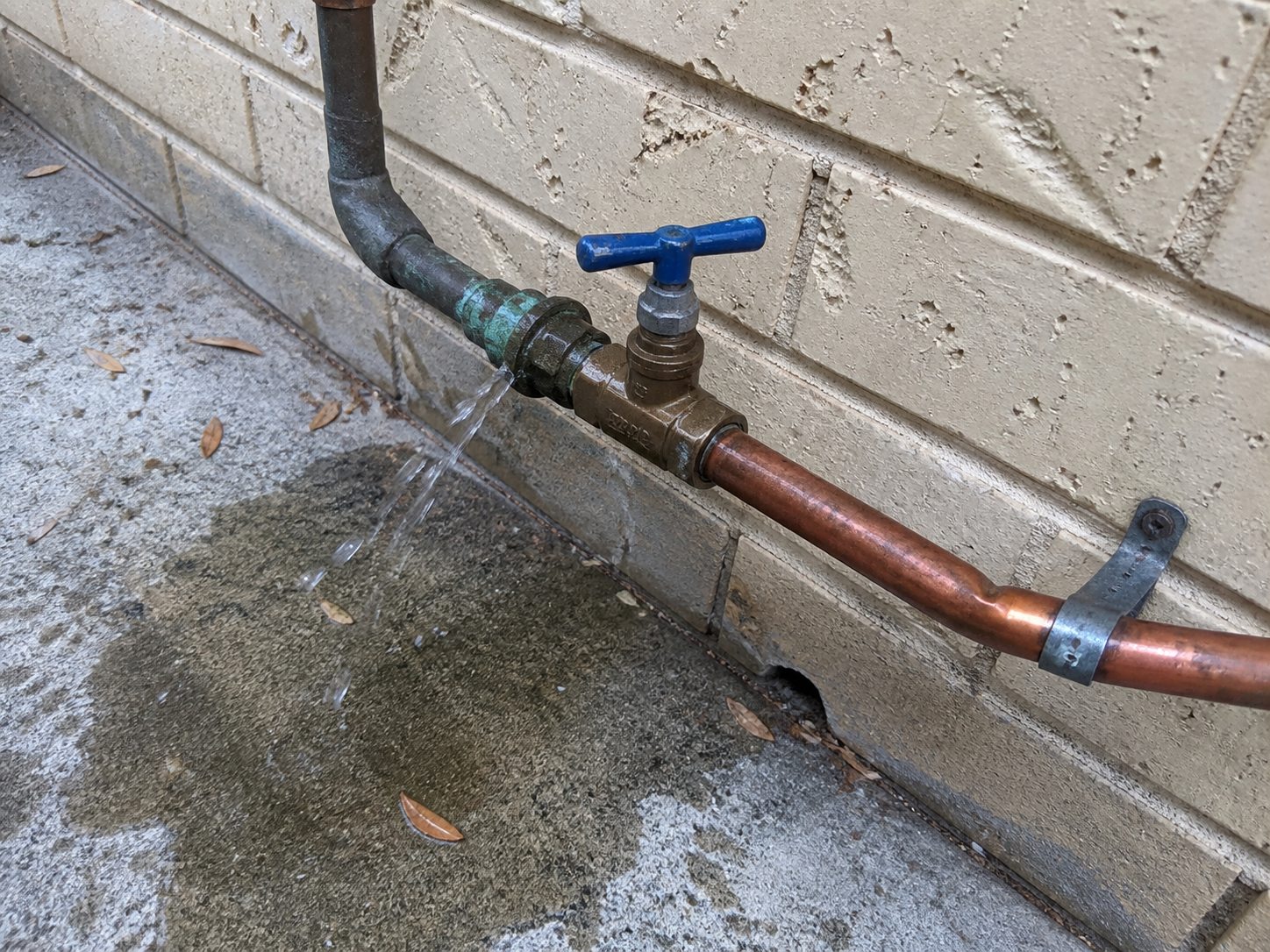 Exterior copper connection leaking beside a weathered residential wall